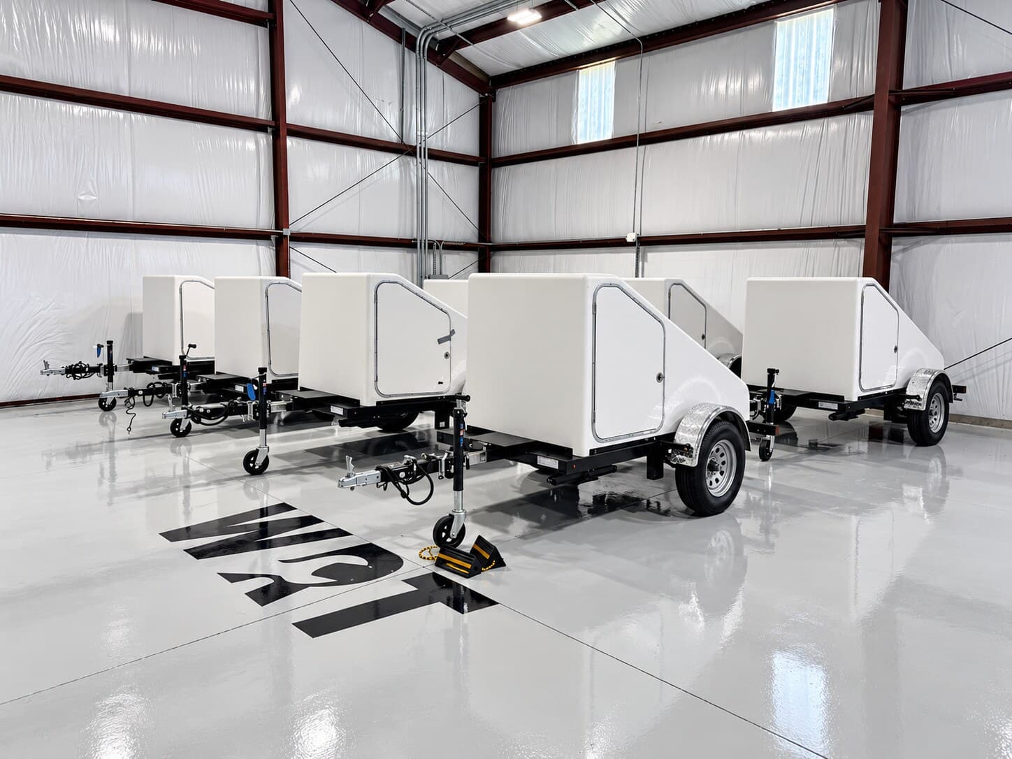 Completed WRT fiberglass shells mounted on trailers, lined up on the WRT warehouse floor beside the painted WRT logo