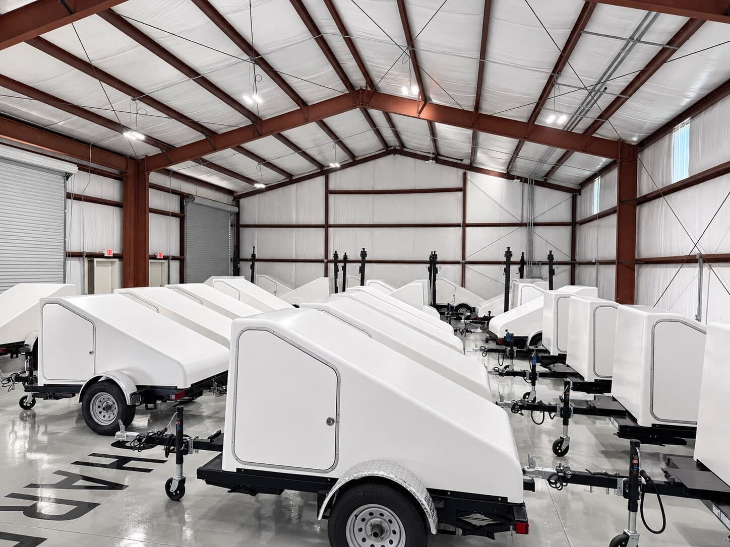 Rows of completed WRT trailers with white fiberglass shells and camera masts, staged in the WRT warehouse